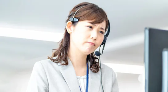 顧客からの電話対応で表情を曇らせるコールセンターの担当者